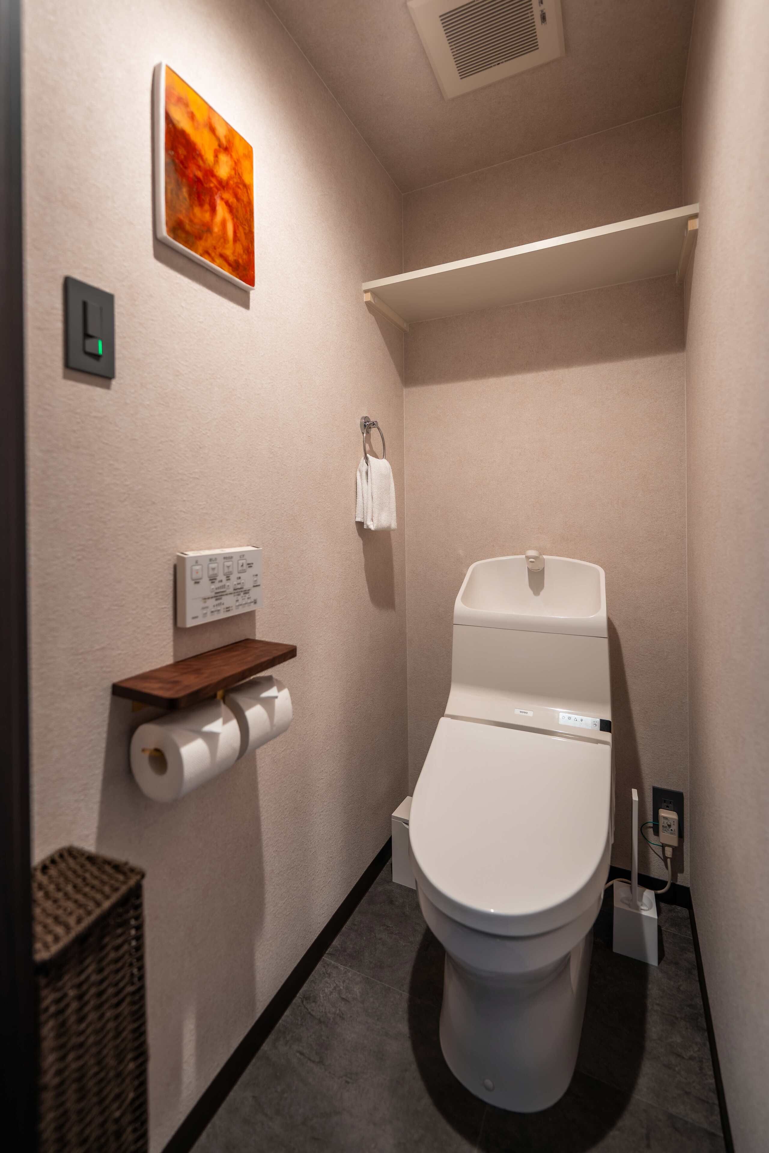 Un baño moderno con inodoro, dispensador de toallas de papel en la pared, una pequeña repisa y un perchero.