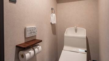 Un baño moderno con inodoro, dispensador de toallas de papel en la pared, una pequeña repisa y un perchero.