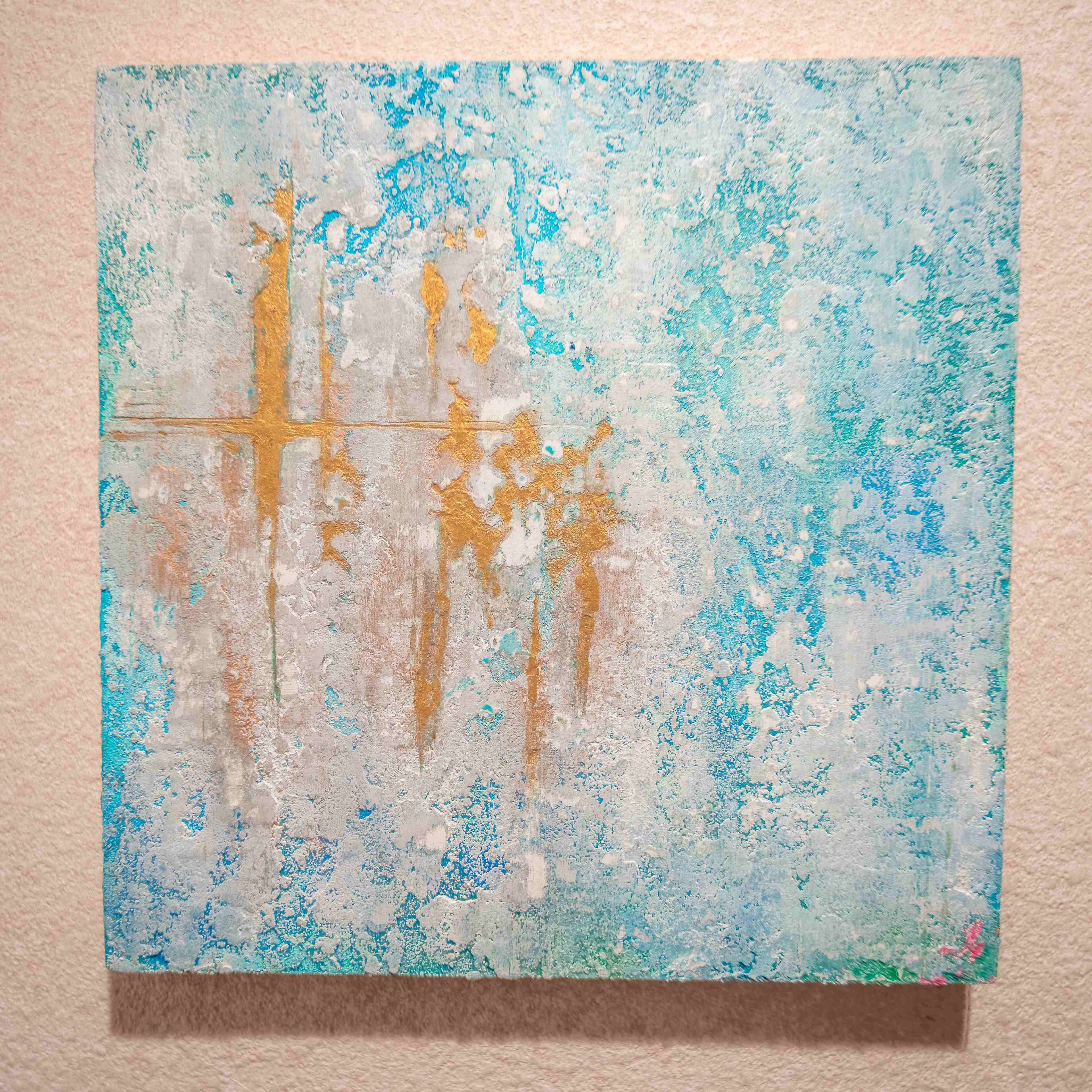 Un tableau carré à la surface texturée, présentant des formes abstraites dans les tons de bleu et d’or.