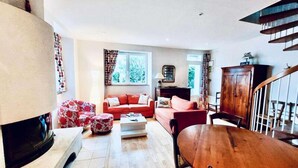 A living room with a fireplace, a red sofa, a wooden dining table, and a staircase. - House in Tregastel Near Pink Granite Coast (Tregastel)