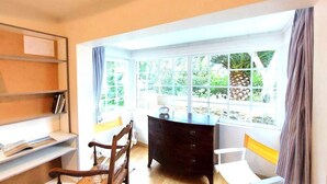 A room with a desk, two chairs, a bookshelf, and a large window with a view of greenery. - House in Tregastel Near Pink Granite Coast (Tregastel)