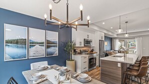 A modern kitchen with a central island, white cabinetry, and a dining area with a table set for four. - Classic Modern 4BR Nearby DT with Hot tub & Pool (Canmore)