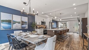 A modern kitchen with a central island, bar stools, and a dining area with a wooden table and chairs. - Classic Modern 4BR Nearby DT with Hot tub & Pool (Canmore)