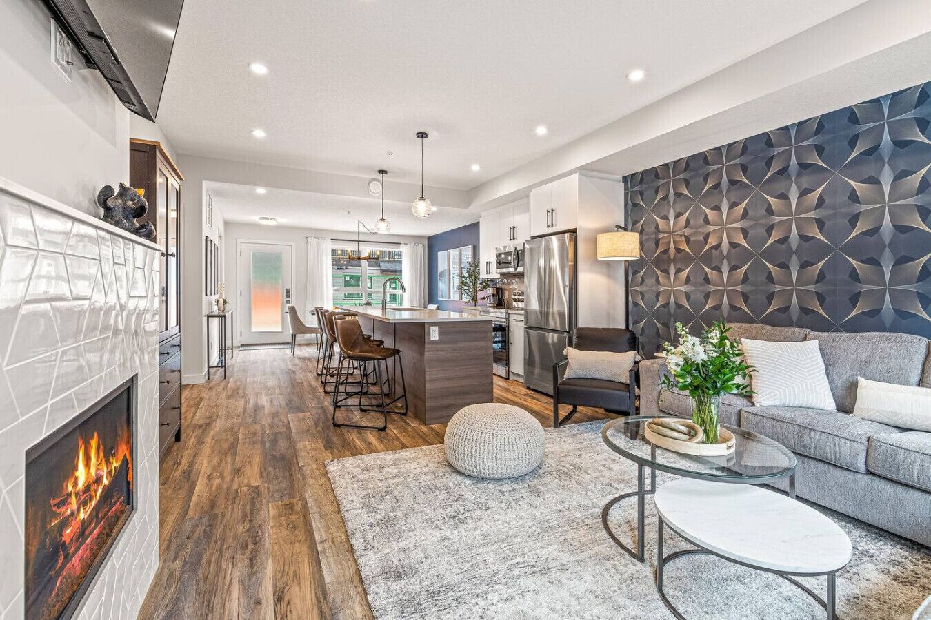 A modern kitchen with a central island, a dining area with chairs, a sofa, and a fireplace.