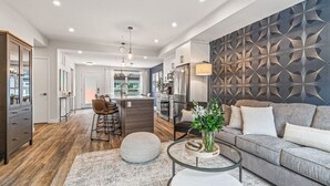 A modern living room with a grey sofa, a coffee table, and a dining area with bar stools. - Classic Modern 4BR Nearby DT with Hot tub & Pool (Canmore)