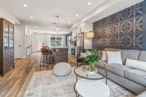 A modern living room with a grey sofa, a round coffee table, and a bar area with stools. - Classic Modern 4BR Nearby DT with Hot tub & Pool (Canmore)