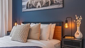A bedroom with a bed, pillows, a headboard, bedside tables, a lamp, and a wall-mounted picture. - Classic Modern 4BR Nearby DT with Hot tub & Pool (Canmore)