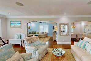 A spacious living room with a light blue sofa, a white sofa, and a wooden coffee table. There is a dining area with a chandelier and a kitchen in the background. - Luxury Home, Dog Friendly, Ocean Views, Steps to the Ocean and Downtown Wrightsville Beach (Wrightsville Beach)