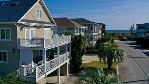 Une propriété située en bord de mer, comprenant une maison à deux étages dotée d’un balcon avec coin salon extérieur et d’une véranda.