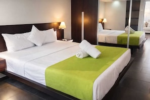 A hotel room with a large bed, a nightstand, a mirror, and a green accent on the bed.