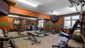 Een sportschool met diverse trainingsapparaten, een televisie en een raam dat natuurlijk licht biedt.