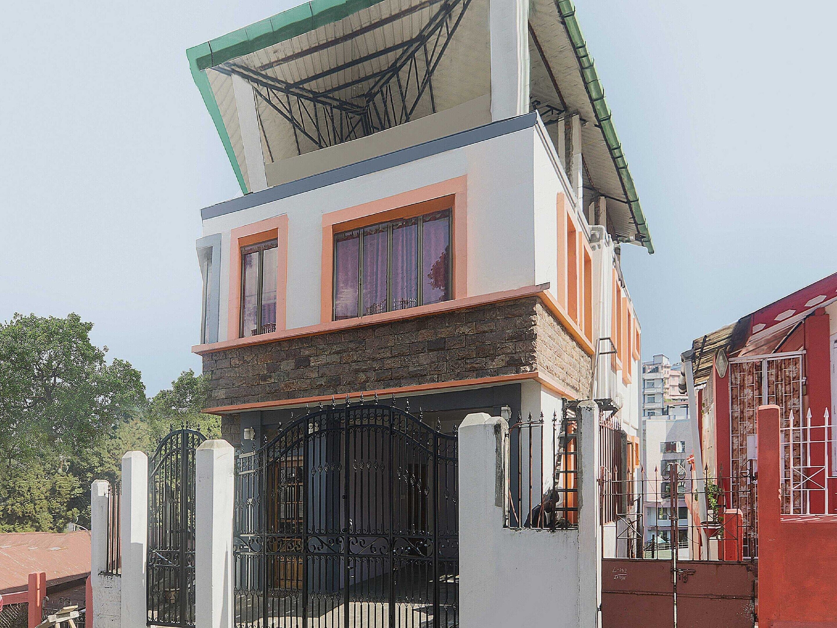 A two-story building with a stone facade, a metal gate, and a red building adjacent to it.