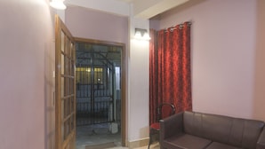 A room with a brown leather sofa, a red chair, a wooden door leading outside, and a red patterned curtain. - Hotel O by OYO Am Bed And Breakfast (Shillong)