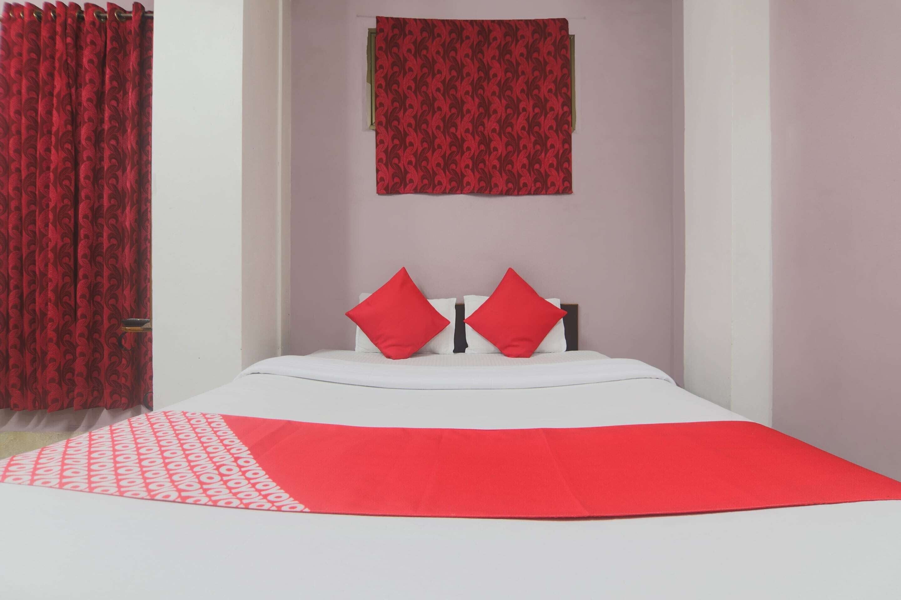 Un lit avec un matelas blanc et des oreillers rouges, un rideau rouge à motifs et une couverture rouge.