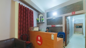 A reception area with a wooden desk, a red curtain, a brown leather couch, and a blue chair. - Hotel O by OYO Am Bed And Breakfast (Shillong)