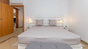 A bedroom with a bed, bedside lamps, a wardrobe, and an air conditioning unit. - Villa Sheike V3 com Piscina Privada (Tavira)