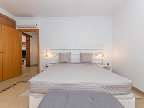 A bedroom with a bed, bedside lamps, a wardrobe, and an air conditioning unit. - Villa Sheike V3 com Piscina Privada (Tavira)
