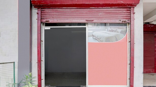Un edificio con fachada roja y blanca, una puerta con contraventanas cerradas y una pequeña planta en maceta en el suelo.