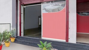 Un edificio de fachada roja y blanca, con puerta corredera de vidrio y plantas en macetas al frente.