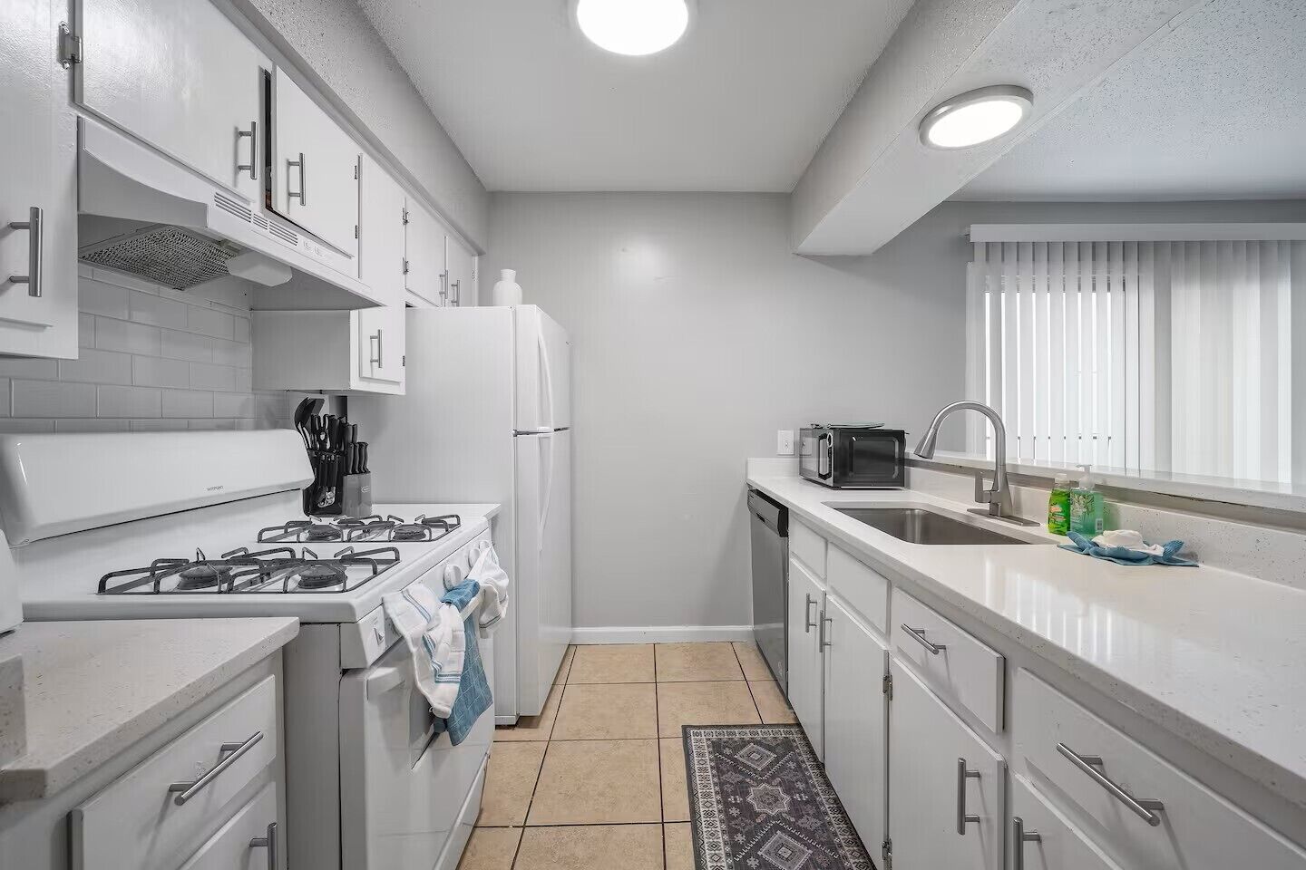 Een moderne keuken met witte kasten, een gasfornuis, een koelkast, een magnetron en een spoelbak.