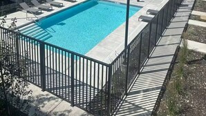 A rectangular swimming pool with a black metal fence, surrounded by a paved deck. - Chick & Cozy Haven near Banff with Hot tub & Pool (Canmore)