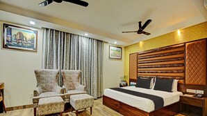 Une chambre à coucher avec un grand lit, deux fauteuils, une tête de lit en bois et un ventilateur de plafond.