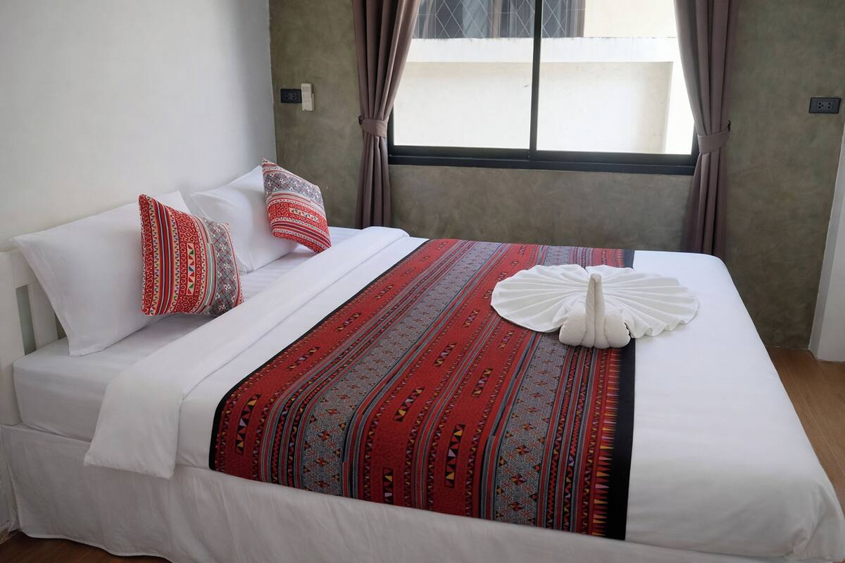 A hotel room with a bed, pillows, a decorative towel, and a window with curtains.