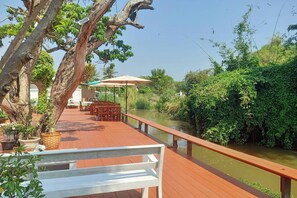 Un muelle de madera con un banco blanco, rodeado de follaje y un río.