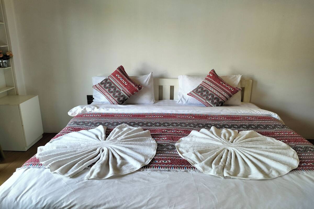 A neatly made bed with patterned pillows, a decorative towel, and a red and white patterned bedspread.