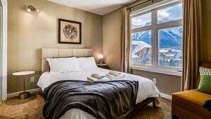 Et hotelværelse med en seng, sengeborde, et vindue med udsigt til et bjerg og et billede i ramme på væggen.
