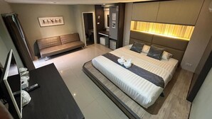 Une chambre d’hôtel moderne, dotée d’un grand lit, de tables de chevet, d’un bureau avec une chaise, d’un banc et d’un miroir.