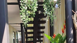 Un espace extérieur aménagé avec des chaises et des tables en bois, entouré de plantes en pot et d’une clôture en bambou.