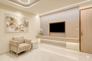 A modern reception area with a sofa, a small side table, a TV, and a wooden door. - Hotel Aero Home Prime (New Delhi)