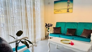 Un salon avec un canapé de couleur turquoise, une table basse blanche et une plante décorative.