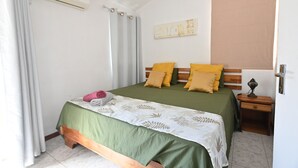 Une chambre à coucher comprenant un lit, des rideaux, un climatiseur fixé au mur, une table de chevet avec une lampe et une œuvre d’art décorative accrochée au mur.