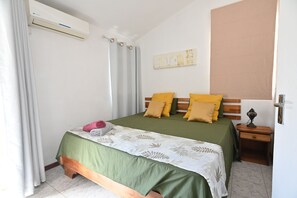 A bedroom with a bed, curtains, a wall-mounted air conditioner, a bedside table with a lamp, and a wall art piece. - 4BR Villa with A/C -High speed Internet • 20mts from Beach • Rooftop Sunset Spot (Flic en Flac)