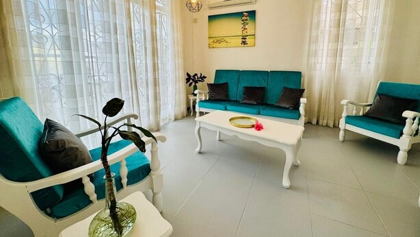 Un salon avec un canapé blanc, un canapé de couleur turquoise et une table basse blanche. On peut voir un vase avec une plante sur la table basse.