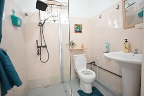 A bathroom with a glass shower enclosure, a toilet, a sink, and a small shelf with toiletries. - 4BR Villa with A/C -High speed Internet • 20mts from Beach • Rooftop Sunset Spot (Flic en Flac)