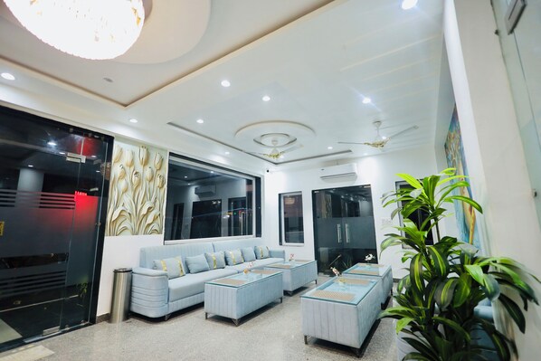 A modern living room with a sofa, ottomans, and a large plant. - BUDDHA DHAM (Vrindavan)