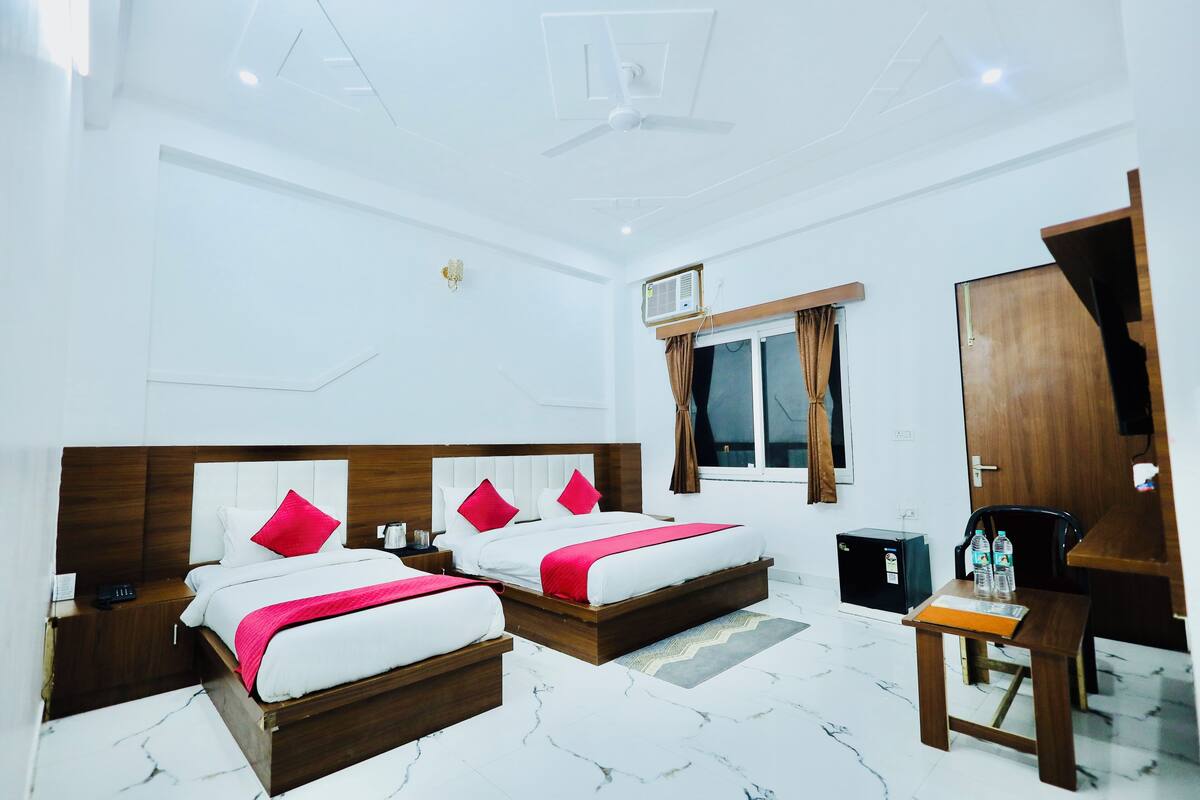 Une chambre d’hôtel avec deux lits, un bureau, une chaise, une petite table, une armoire et une fenêtre avec des rideaux.