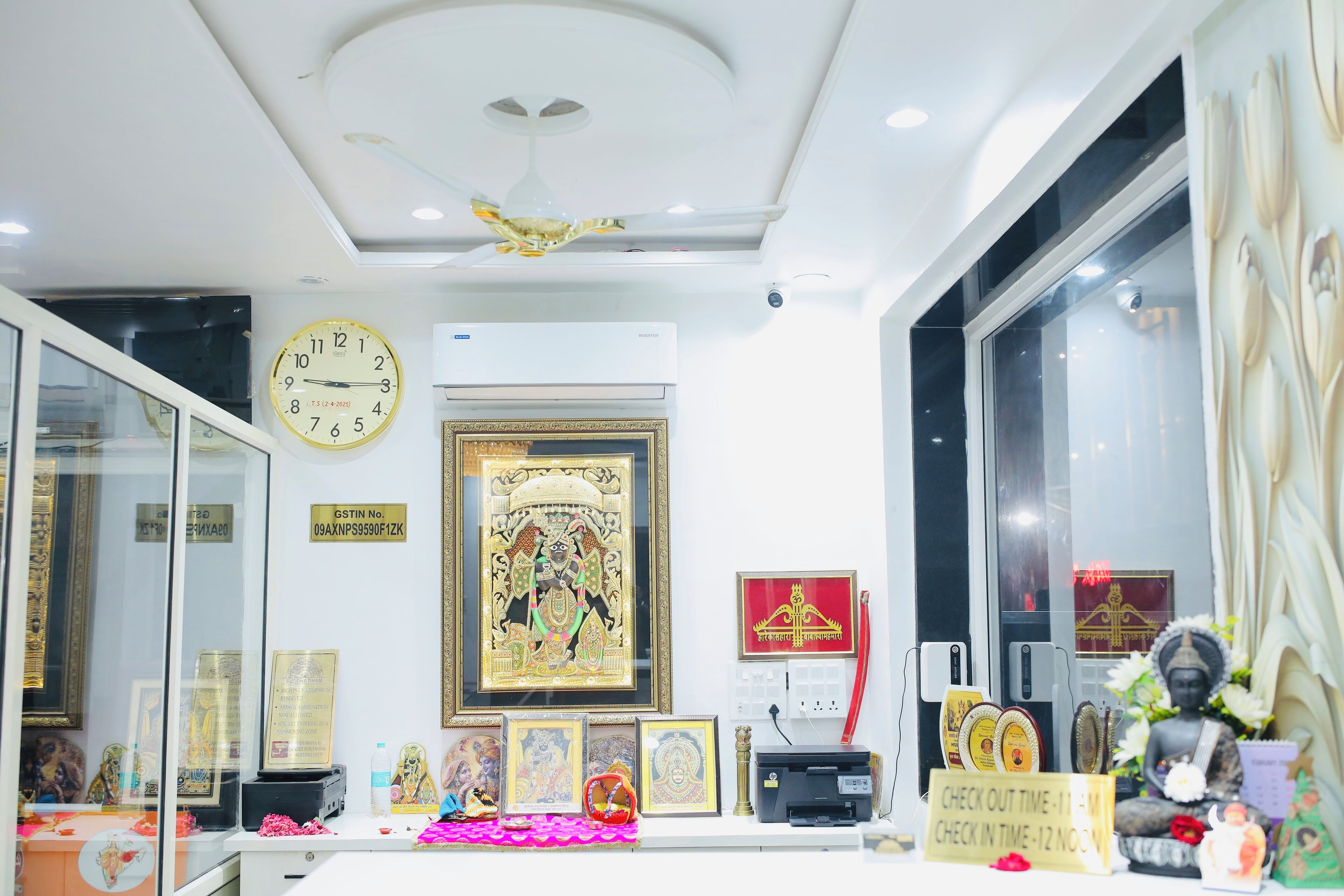 Une pièce dotée d’un ventilateur de plafond, d’une horloge murale, d’œuvres d’art encadrées et d’une statue de Bouddha.