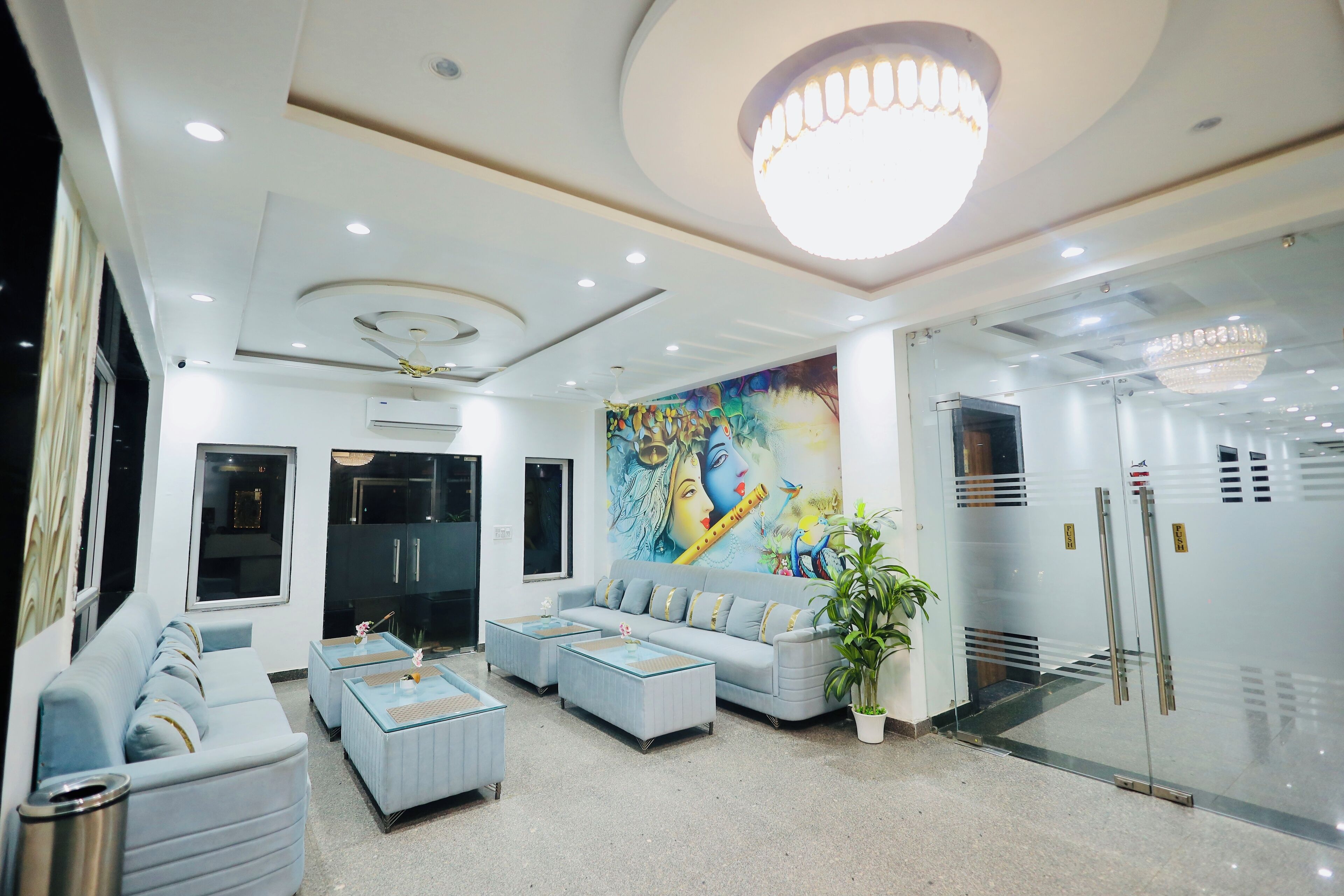 A modern hotel lobby with a light blue sofa, two matching ottomans, a large mural, and a glass door entrance.