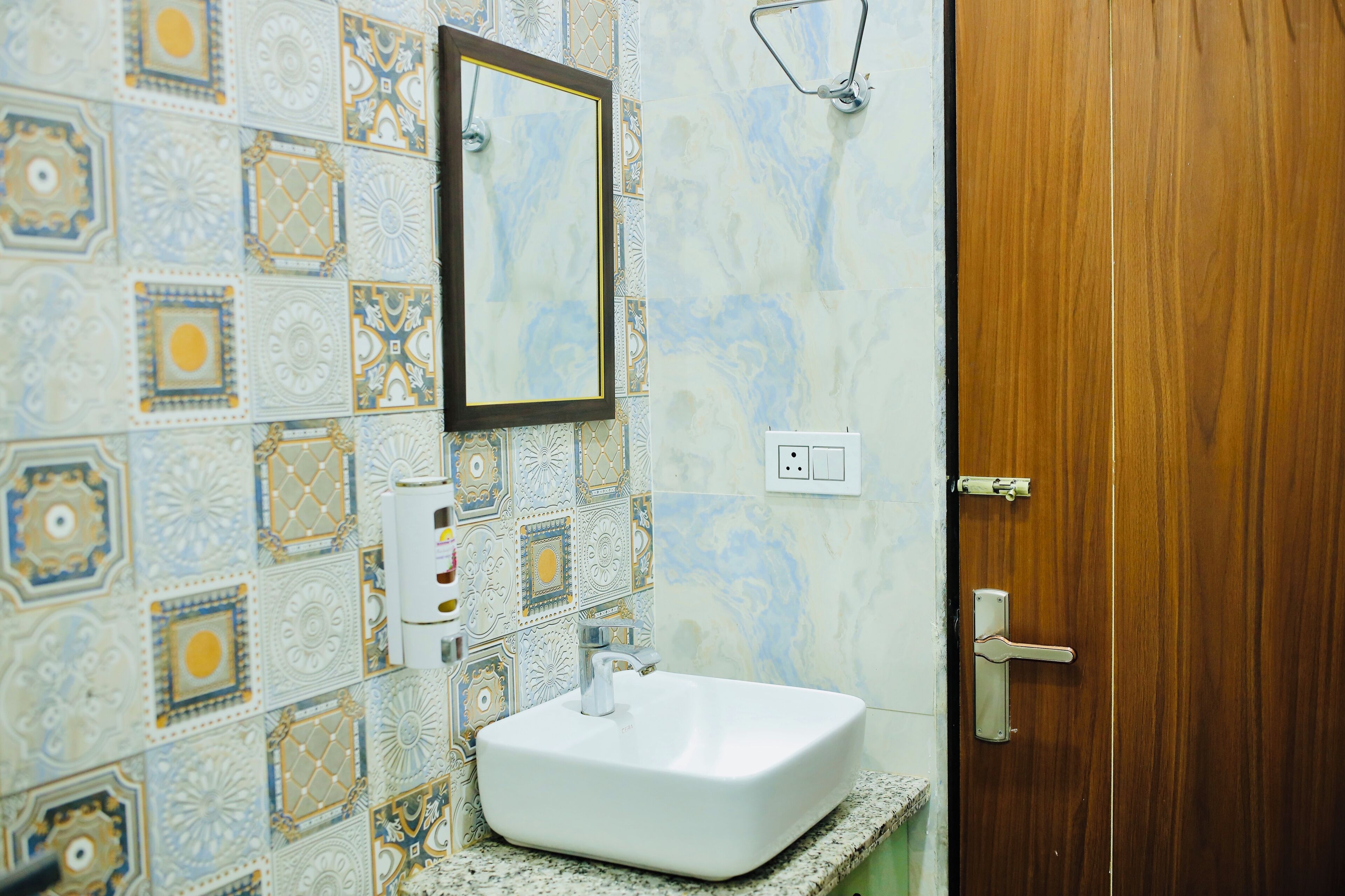 Un baño con lavamanos blanco, un espejo y una puerta de madera.