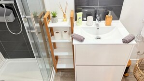 Une salle de bain moderne avec une douche à parois de verre, un lavabo blanc avec un miroir et un meuble-lavabo en bois.