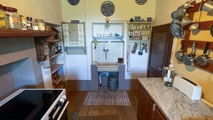 Uma cozinha compacta com forno embutido, pia e fogão. Há prateleiras com potes e um suporte para panelas pendurado.