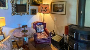 Um quarto aconchegante com uma poltrona de couro, uma mesinha redonda com castiçal, lareira e quadros nas paredes.