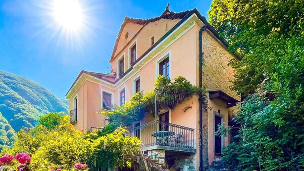 Uma casa de dois andares com varanda, rodeada por vegetação exuberante e flores.