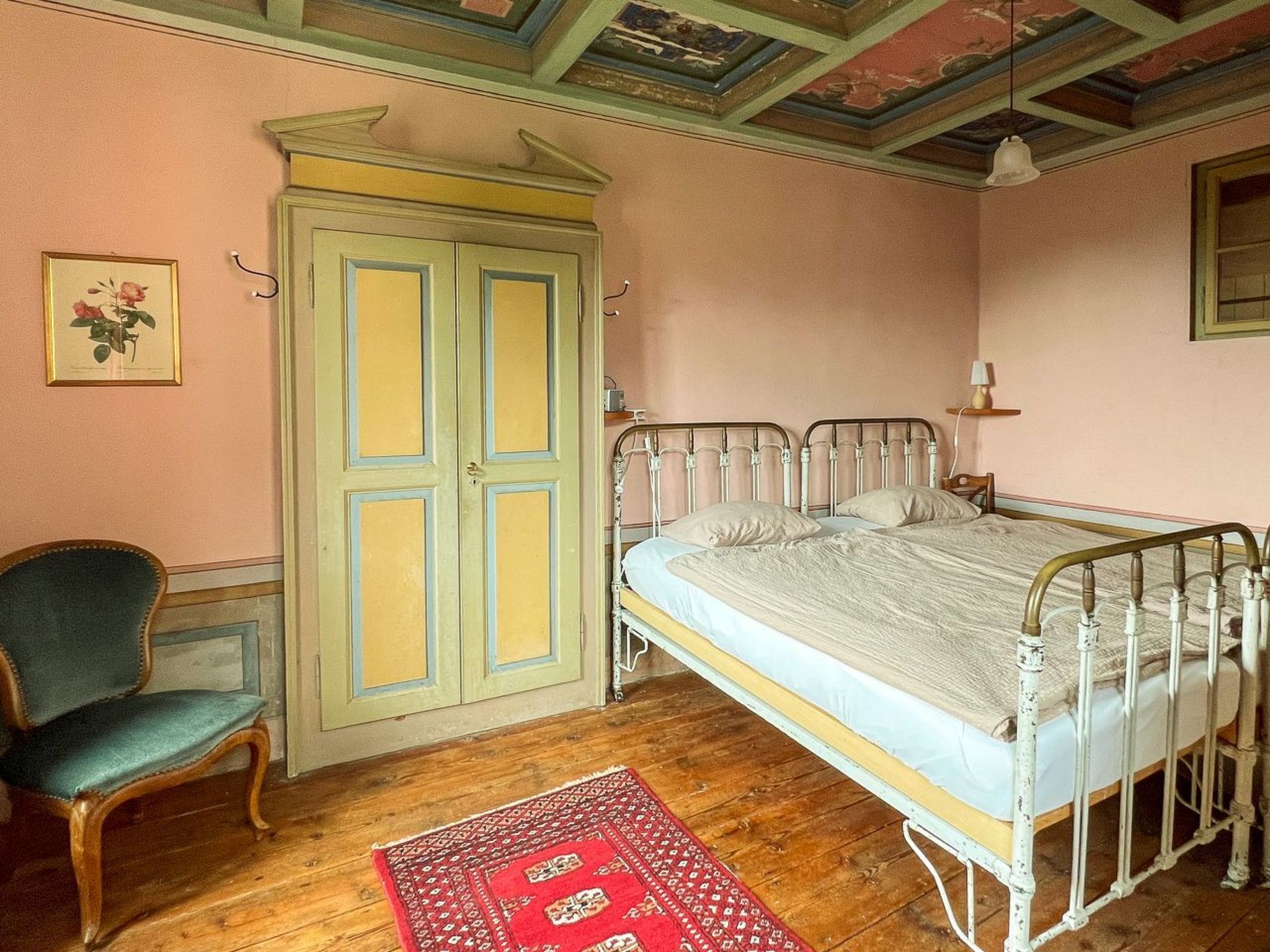 A bedroom with a bed, a chair, a wardrobe, and a red rug.