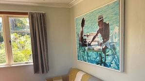 A room with a sofa, a wooden table, and a painting of two people by a pool. - Tranquil Early 1900s Retreat in Auckland with Free Parking (Whenuapai)