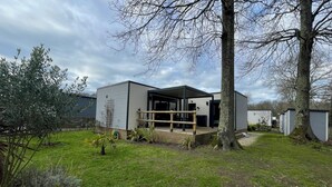 Een modern, twee verdiepingen tellend huis met een overdekte patio, omgeven door een verzorgde tuin en bomen.